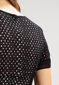 Närbild av en person som bär en svart kortärmad topp med mönstrad utskuren tyg och en dragkedja på den övre delen av ryggen.