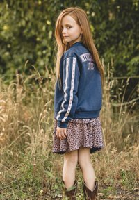 Denimjack met de opdruk "University of Love" en gestreepte mouwen met roze hartjes. Bloemenrok en bruine cowboylaarzen maken de outfit compleet.