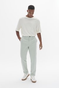 Pantalon droit vert clair en coton doux, associé à une chemise crème à manches courtes et des baskets blanches avec des semelles marron.