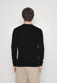 Felpa nera a maniche lunghe con scollo a girocollo e polsini a costine. Realizzata in tessuto morbido, leggermente aderente, con un design pulito e minimalista.