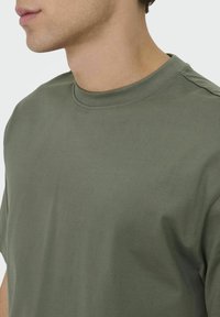 Olive green cotton t-shirt with a crew neck, short sleeves, and visible stitching detail. Soft texture with a relaxed fit silhouette.