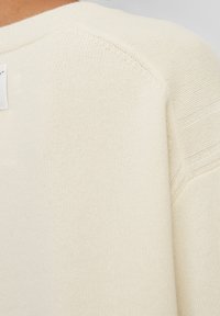 Pull en maille crème claire avec un col rond côtelé et des panneaux texturés aux épaules. Tissu doux et lisse avec un léger éclat.