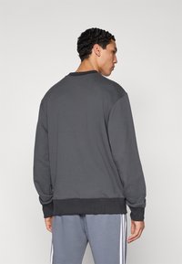 Hanorac gri închis cu decolteu rotund, tiv și manșete striate. Prezintă o textură netedă și o croială lejeră.