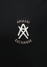 Μαύρο ύφασμα με λευκό κεντημένο λογότυπο Armani Exchange που παρουσιάζει στυλιζαρισμένα γράμματα "A" και "X" και κείμενο με το όνομα της μάρκας σε καμπύλη πάνω και κάτω.