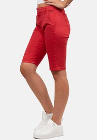Rode denim bermuda shorts met een aansluitend ontwerp, zijzakken en een knoopsluiting. Gepaarde met witte sneakers voor contrast.