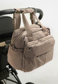 Beige gevoerde tas met twee verstelbare stoffen riemen, een voorvak met ritssluiting en een gladde textuur, bevestigd aan het handvat van een kinderwagen.