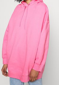 Överdimensionerad rosa hoodie i mjukt tyg med dragsnodd i huvan och ribbade ärmslut; avslappnad passform med en bekväm, avslappnad design.