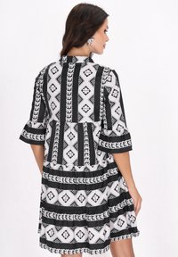 Mustavalkoinen kuviollinen mekko, jossa on levenevä muotoilu, geometrisiä muotoja, röyhelösleevejä ja kerroksellinen helma.