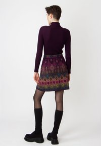 Dunkelvioletter Strickrollkragenpullover mit einem gemusterten Minirock, der mehrfarbige geometrische Designs zeigt, und schwarzen kniehohen Plateaustiefeln.
