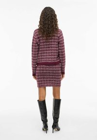 Burgunder farge strikket genser og skjørt sett med en teksturert rutemønster. Akkompagnert av svarte høye stiletto støvler.