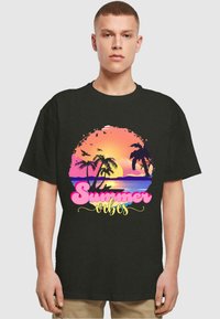 Zwart T-shirt met een grafisch ontwerp van een zonsondergang boven palmbomen, met de tekst "Summer Vibes" in roze en geel, gedrukt op de voorkant.