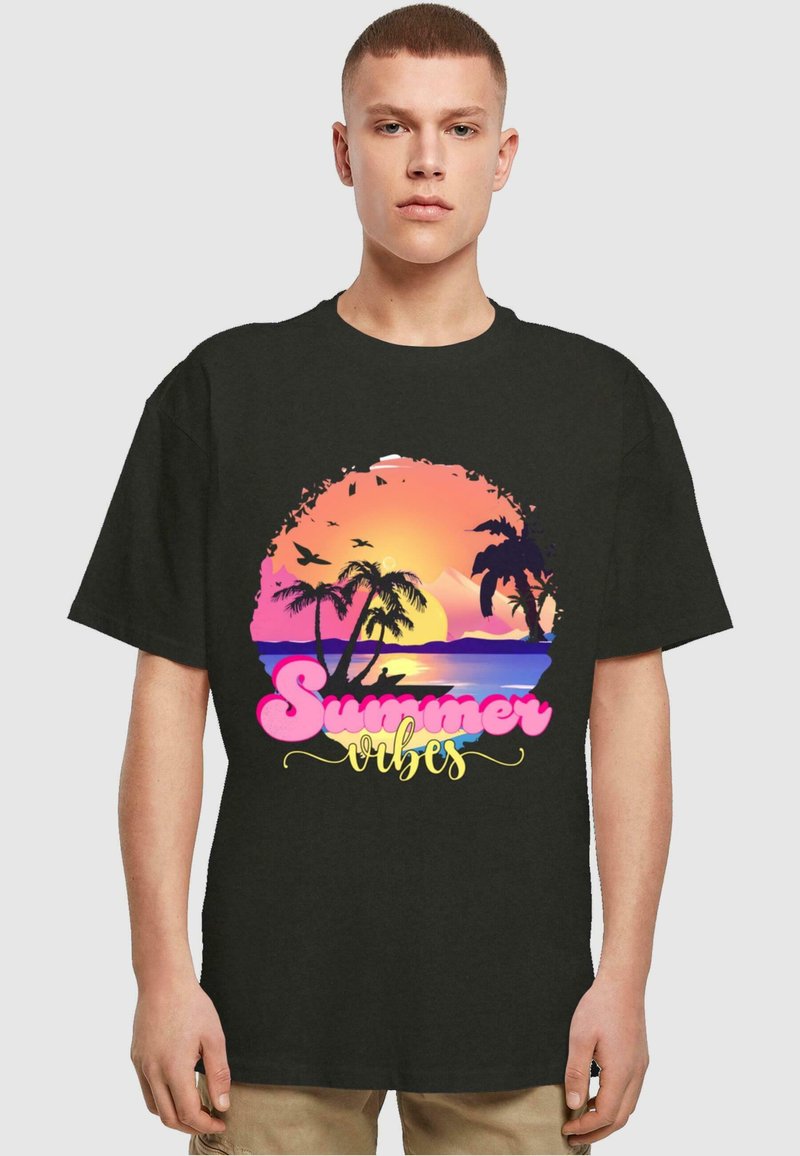 Zwart T-shirt met een grafisch ontwerp van een zonsondergang boven palmbomen, met de tekst "Summer Vibes" in roze en geel, gedrukt op de voorkant.