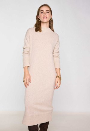 Abito in maglia beige con collo alto, maniche lunghe e polsini a costine. Presenta una silhouette dritta e un orlo che arriva fino a metà polpaccio.