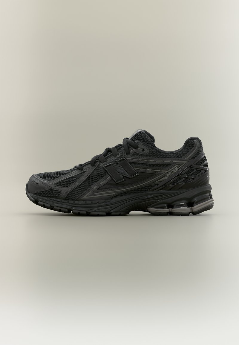 Baskets de sport noires avec tige en mesh, fermeture lacée, semelle coussinée et logo de la marque sur le côté, présentées sur un fond uni.