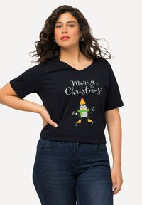 Camiseta negra de cuello en V con un gráfico festivo de "Feliz Navidad" y un pingüino de dibujos animados que lleva un sombrero y una bufanda. Textura suave, corte casual.