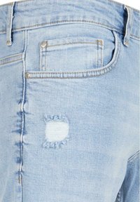 Jeans de mezclilla azul claro con un parche desgastado de bordes deshilachados, bolsillos traseros y detalles de costura estándar a lo largo de las costuras.