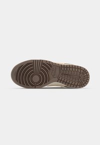 Nike sneaker sole featuring a textured brown rubber bottom with circular patterns and a logo. The shape is flat with raised grip lines.