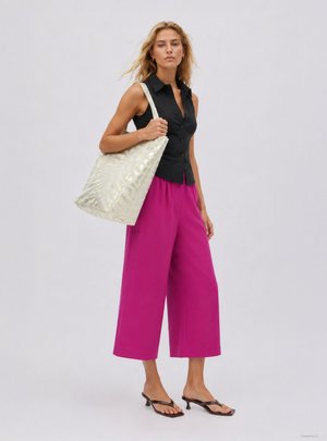 Donna che indossa una camicia nera senza maniche con bottoni, pantaloni larghi magenta, sandali neri con tacco, porta una grande borsa a tracolla beige chiaro.