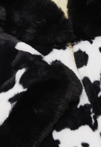 Cappotto in finta pelliccia bianco e nero con motivo a macchie di mucca. Texture morbida con un colletto in finta pelliccia nera e un dettaglio di chiusura a gancio.