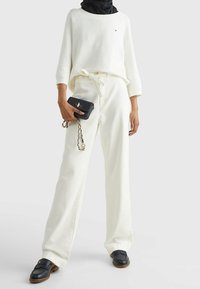 Vit, långärmad tröja och vida byxor, båda i mjukt tyg. Svart handväska med kedjerem, bärs med loafers. Ren, avslappnad stil.