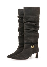 Botas altas, desgastadas, de ante negro con punta afilada, textura sutil, un tacón delgado y un acento decorativo dorado con una correa negra.