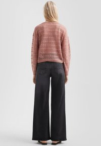 Helles rosa, locker gestricktes Sweatshirt mit einem perforierten Design, kombiniert mit hoch taillierten, weit geschnittenen schwarzen Jeans. Beide Teile haben eine lässige Passform.