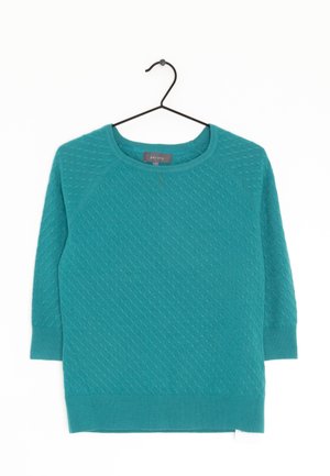 Miętowo teksturowany sweter dziany z rękawami do połowy przedramienia zawieszony na czarnym wieszaku na białym tle.