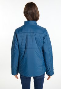 Giacca isolante blu con design trapuntato, colletto alto e maniche lunghe. Tessuto liscio e finitura leggermente lucida.