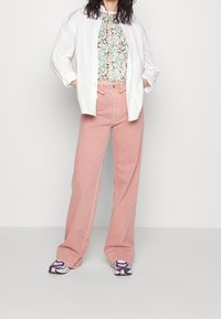 Un pantalon large rose clair associé à un top à manches courtes à imprimé floral et une chemise blanche surdimensionnée, complété par des chaussures de sport à motifs.