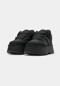 Svart plattformssneakers laget av teksturert syntetisk materiale med tykke såler, med kontrastsnører og forsterkede tåkapper.