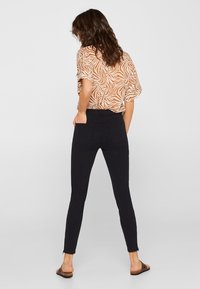 Czarne obcisłe jeansy z tylnymi kieszeniami, zestawione z pomarańczowo-białą bluzką w wzory. Tkanina wydaje się elastyczna i dopasowana.