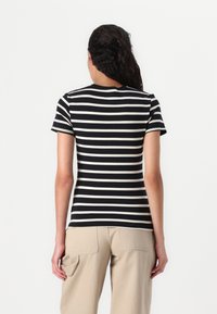 Top a maniche corte bianco e nero a righe, con scollatura rotonda, taglio aderente e texture morbida; abbinato a pantaloni cargo beige.