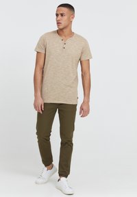 Tan heathered t-shirt med kort ärm, treknapplås, i kombination med olivgröna slim-fit byxor och vita sneakers.