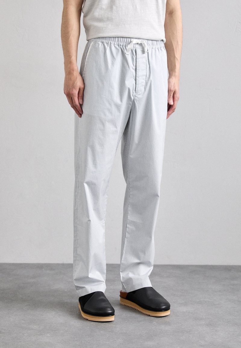 Pantalons légers rayés bleu clair avec une taille élastique et un cordon de serrage. Portés avec des chaussures noires à enfiler avec une semelle en bois.