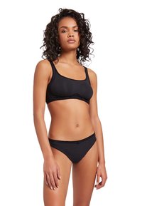 Ensemble de bikini noir comprenant un haut bralette ajusté et épuré avec de larges bretelles et un bas taille basse. Tissu lisse avec un minimum de détails.