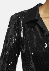 Schwarzes Paillettenhemd mit glänzender Textur, klassischem Kragen und einer Nahaufnahme intricater Paillettenverzierungen auf dem Stoff.