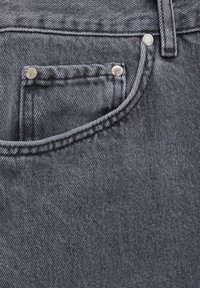 Gros plan sur la poche d'un jean en denim noir avec des coutures visibles et trois rivets argentés, mettant en valeur la texture et les détails du tissu.