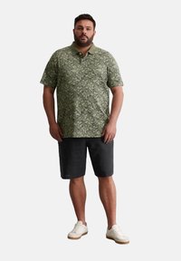 Grünes Poloshirt mit floralem Druck und kurzen Ärmeln, kombiniert mit dunklen Shorts und weißen Sneakers. Lässiges Design mit strukturiertem Stoff.