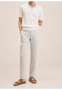 Lekka koszulka polo z krótkim rękawem w kolorze ecru, zestawiona z jasnoszarymi spodniami. Brązowe zamszowe sandały z grubymi paskami dopełniają strój.