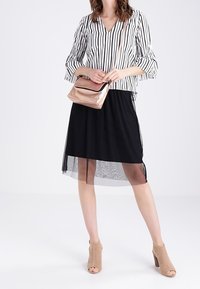 Gonna nera con sovrapposizione trasparente, abbinata a una blusa a righe bianca e nera con maniche a campana. Accessoriata con una pochette metallic rosé e tacchi perforati color cammello.