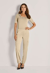 Beige T-shirt met korte mouwen en een decoratieve halslijn, gecombineerd met beige cargo broek met elastische taille en zijzakken, met gebundelde enkelstukken. Zwarte hakken.