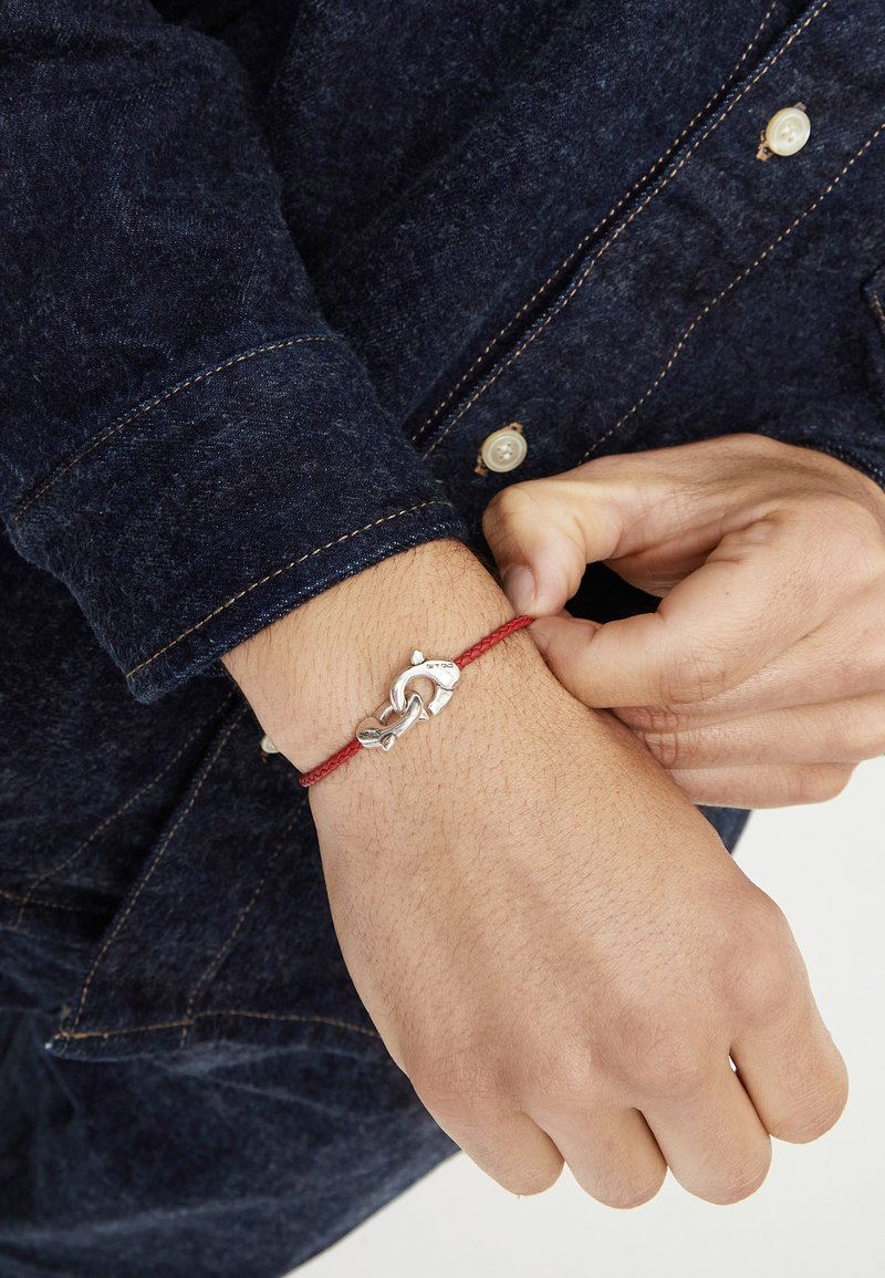 Bracelet en corde rouge avec une fermeture en métal argenté en forme de crochet de pêche. La corde est texturée et la fermeture a une finition polie.