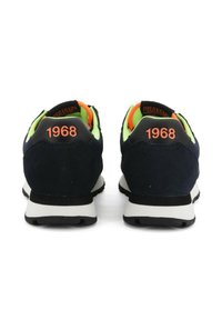 Ein Paar schwarze und neongrüne Sneakers mit oranger "1968"-Aufschrift an der Ferse, von hinten auf einem weißen Hintergrund gezeigt.