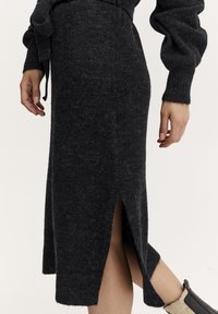Gonna a maglia grigio scuro con uno spacco laterale, vita a costine e tessuto testurizzato, abbinata a un stivale nero aderente sopra la caviglia.