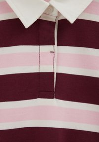 Primer plano de una camiseta de rugby a rayas con franjas horizontales alternas en rojo oscuro, rosa y blanco y un cuello blanco con el botón superior abrochado.