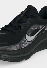 Μαύρο αθλητικό παπούτσι Nike με μαξιλαρωμένη σόλα, μαύρα κορδόνια και ασημένιο λογότυπο swoosh πάνω σε γκρι μαρμάρινο πλευρικό πάνελ.
