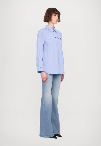 Camicia button-up a righe blu chiaro con due taschini sul petto, abbinata a jeans a zampa d'elefante blu chiaro e scarpe nere a punta.