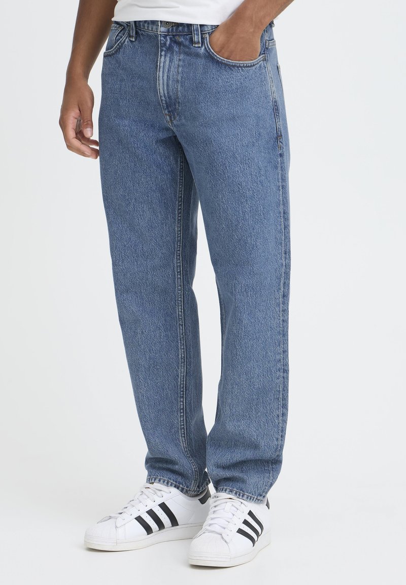 Blå denimjeans med rett snitt og klassisk femlommersdesign, med en falmet finish og synlige sømmer. Kombinert med hvite joggesko.