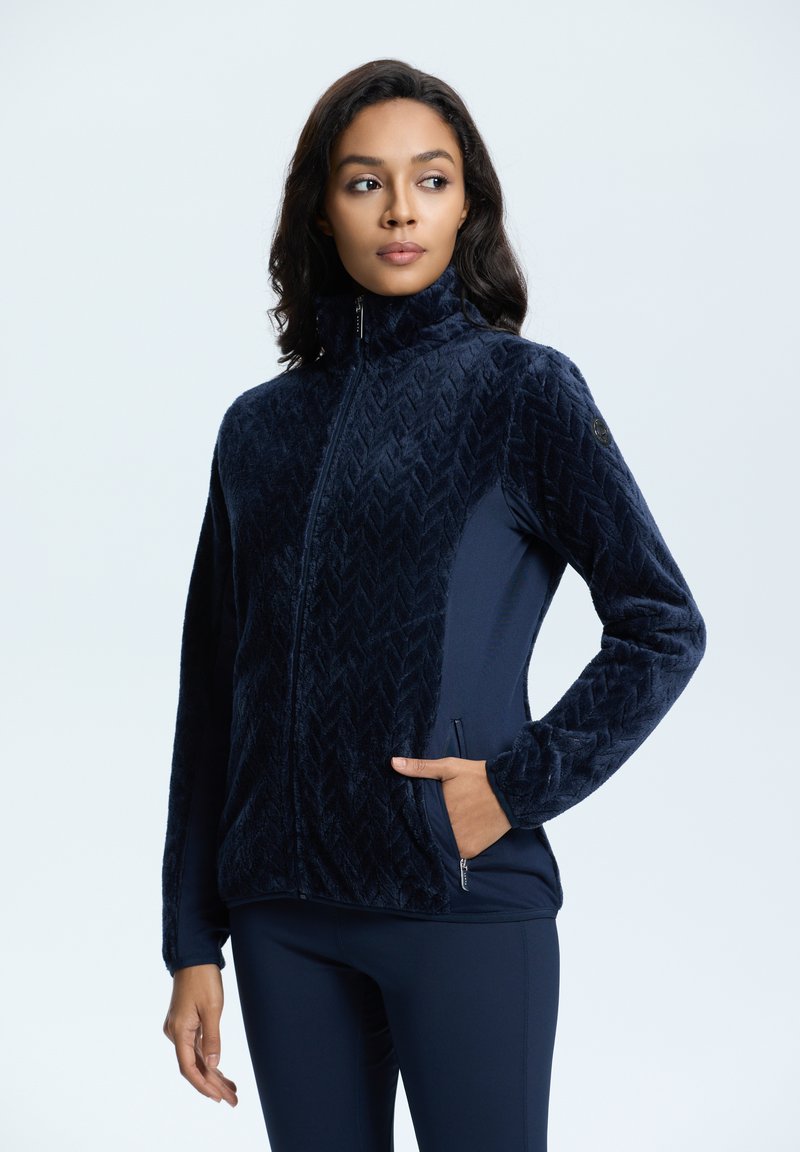 Navyblauwe ritsjas met een chevronpatroon van fleece aan de voorkant en stevige rekbare stof aan de zijkanten. Voorzien van een hoge kraag en zijzakken.