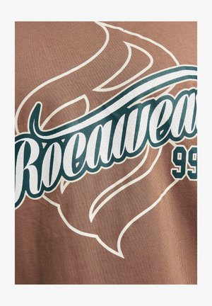Hnedé tkaninové tričko s veľkým bielym a tyrkysovým nápisom "Rocawear 99" s vírivými akcentmi a textúrovaným povrchom.